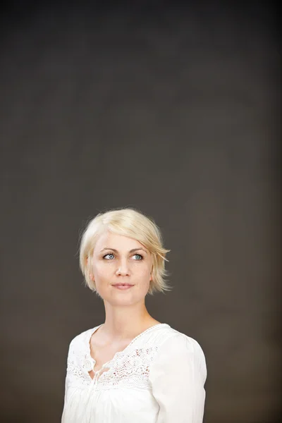 Doordachte blonde vrouw tegen de grijze achtergrond — Stockfoto
