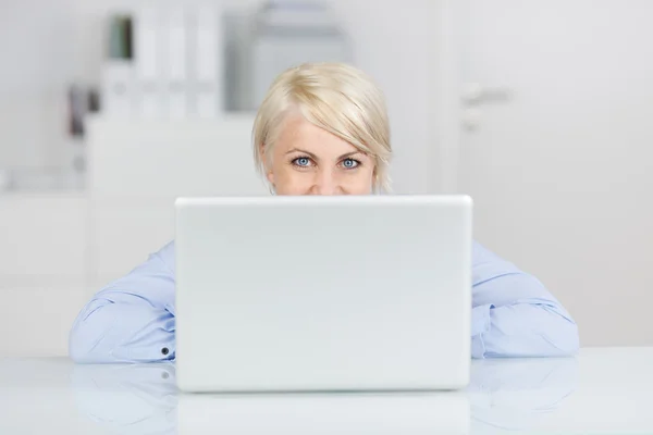 Mulher sorridente no escritório olhando para cima por laptop na mesa — Fotografia de Stock