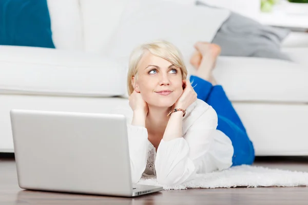 Nachdenkliche Frau mit Laptop entspannt auf dem Boden — Stockfoto