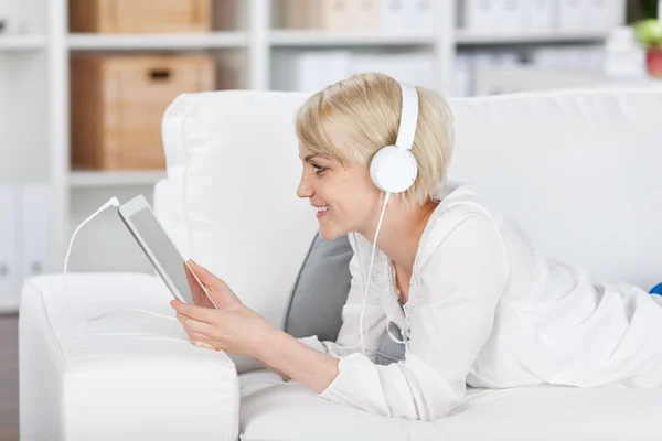 Mulher ouvindo música com fones de ouvido e tablet em casa — Fotografia de Stock