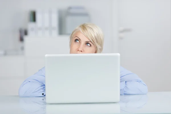 Mujer de negocios reflexiva mirando hacia arriba por el ordenador portátil en el escritorio — Foto de Stock