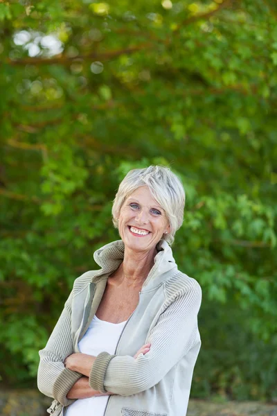 Äldre kvinna med armarna korsade stående i park — Stockfoto