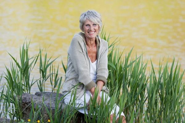 Alegre anciana sentada cerca del lago — Foto de Stock