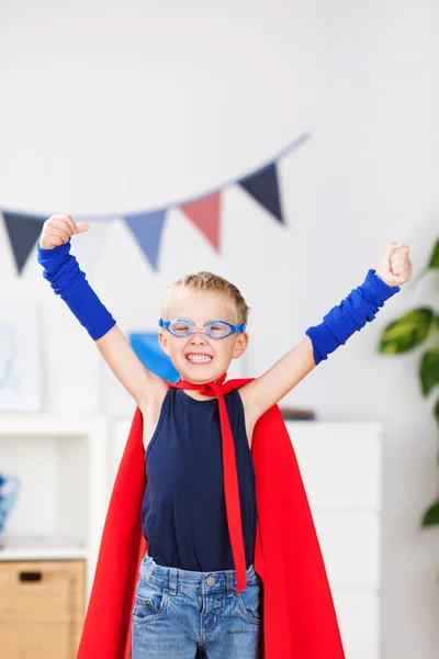 Menino com braços criados em trajes de super herói em casa — Fotografia de Stock