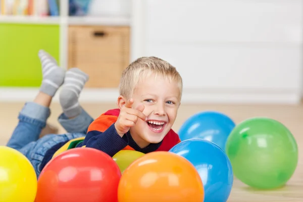 Ragazzo che indica mentendo con palloncini colorati sul pavimento — Foto Stock