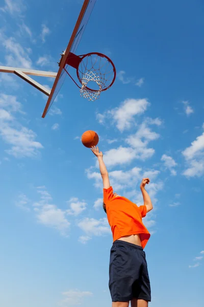 Chlapec hraje basketbal proti modré obloze — Stock fotografie