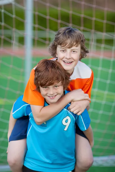 Pojke ger piggyback rida till vän på fotbollsplan — Stockfoto