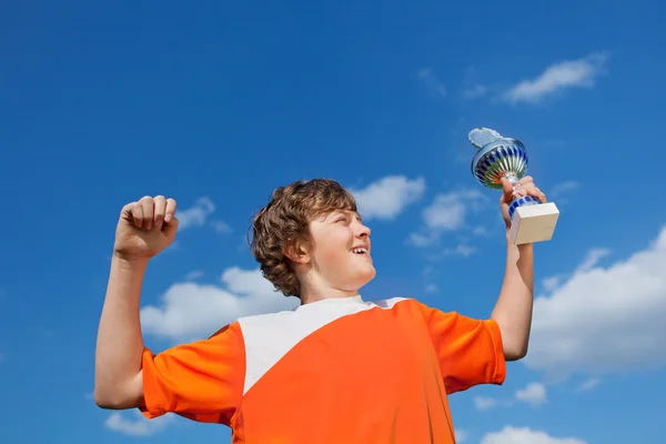 Niño celebrando la victoria mientras sostiene trofeo contra el cielo — Foto de Stock