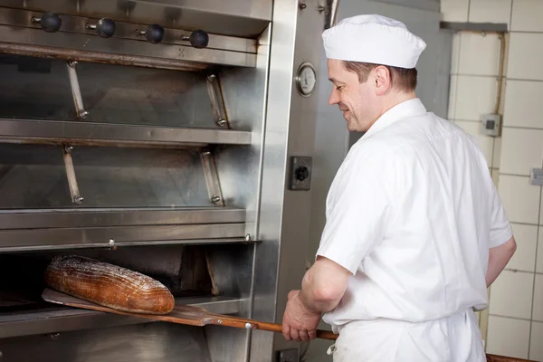 Baker taking bread from the oven — Stock Photo, Image