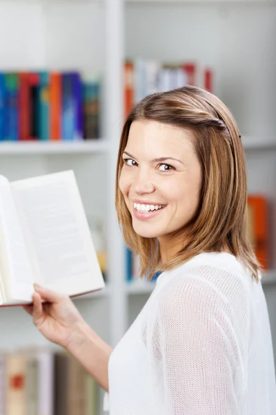 Smiling female standing in front of the bookshelf — Stock Photo, Image