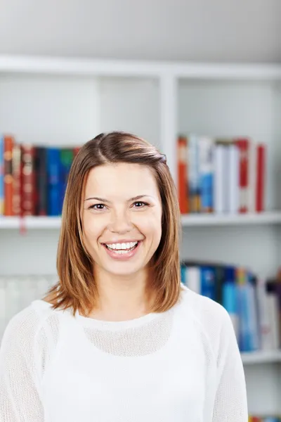 Beautiful woman smiling in front of a book shelf. — Stock Photo, Image