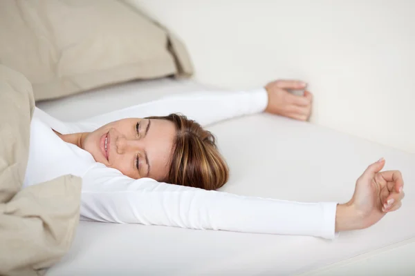 Mulher sorridente que se estende na cama — Fotografia de Stock