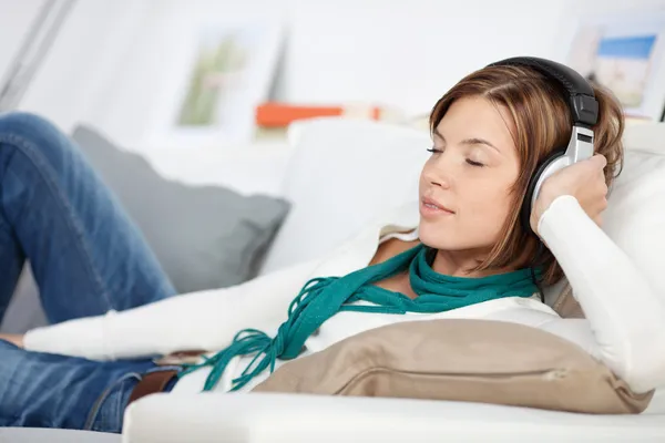 Mulher relaxando em um sofá ouvindo música — Fotografia de Stock