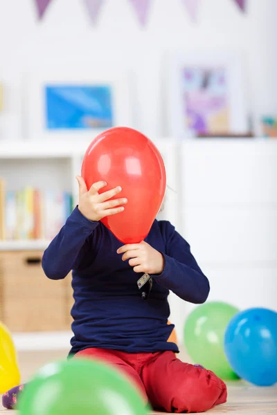 Playful girl hiding behind a red balloon — Stock Photo, Image