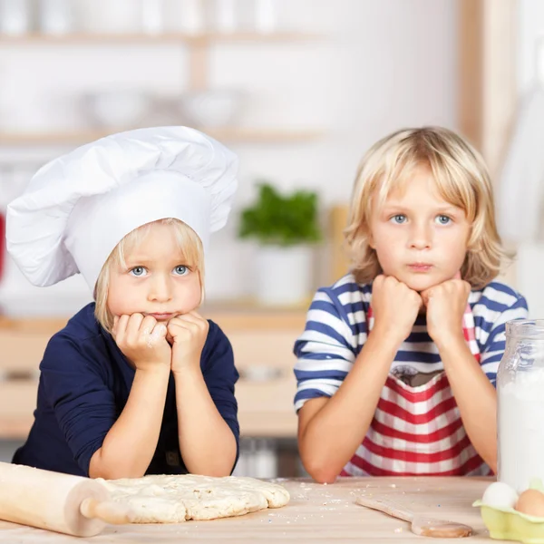 Geschwister schauen weg, während sie sich an Küchentisch lehnen — Stockfoto