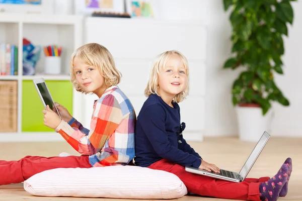 ノート パソコンとデジタル タブレットの枕の上に座っている女の子 — ストック写真