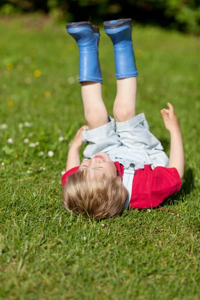 Chlapec s feetup smíchu vleže na trávě — Stock fotografie