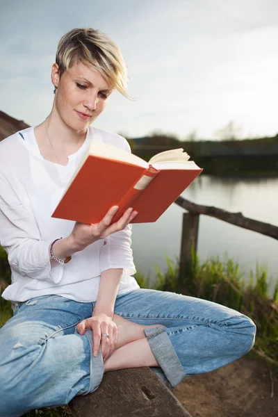 Blond femme lecture livre par lac — Photo