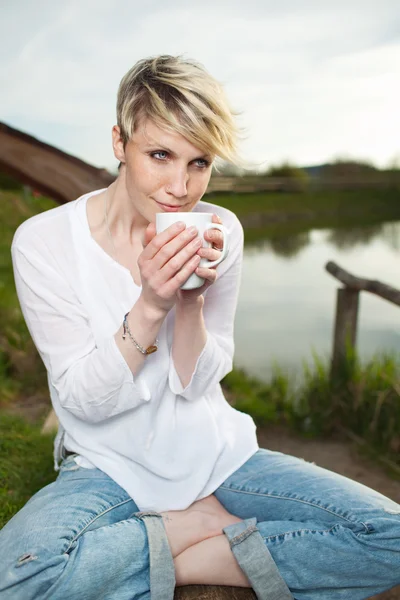 Gölün kıyısında sıcak kahve fincanı tutan kadın — Stok fotoğraf