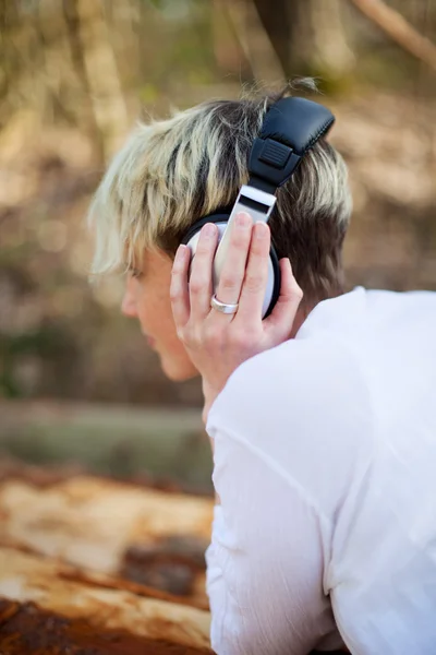 Rückansicht einer Frau mit Kopfhörer auf Baumstamm liegend — Stockfoto
