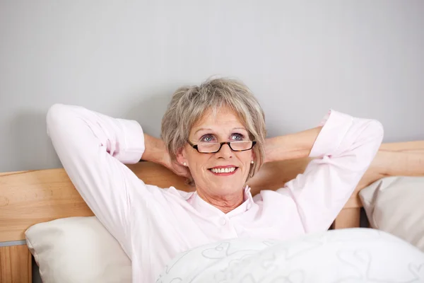 Femme âgée réfléchie avec les mains derrière la tête au lit — Photo