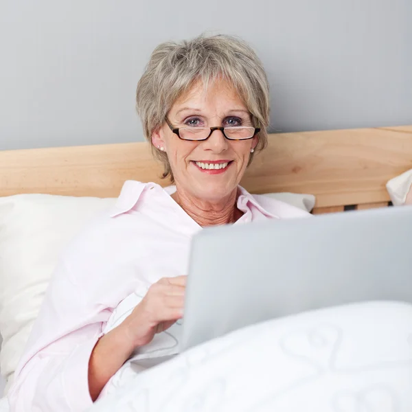 Mulher sênior com laptop deitado na cama — Fotografia de Stock