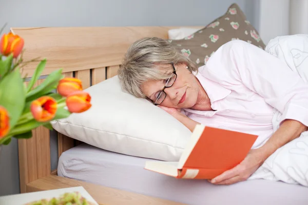 Senior vrouw lezen boek terwijl liggend in bed — Stockfoto