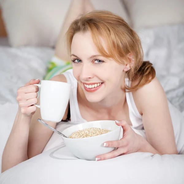 Mulher segurando Muesli tigela e xícara de café enquanto deitado na cama — Fotografia de Stock