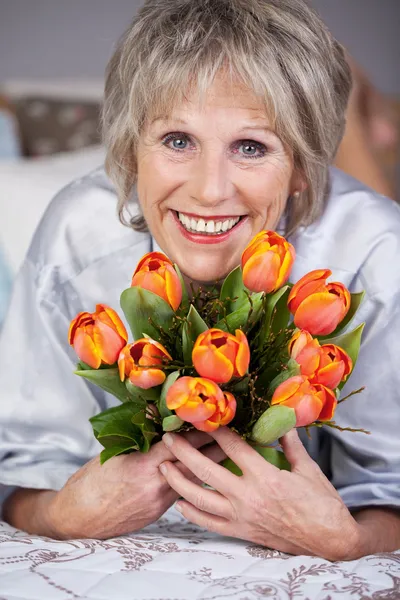 Mujer mayor sosteniendo racimo de tulipanes en la cama Fotos de stock