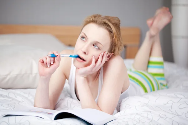 Woman With Book And Pen Looking Away In Bed Stock Photo