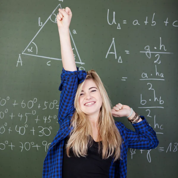 Menina com mão levantada comemorando o sucesso contra o quadro negro — Fotografia de Stock