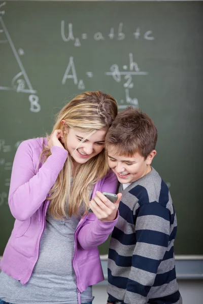 Students Reading Text Message On Cell Phone Against Chalkboard — Stock Photo, Image