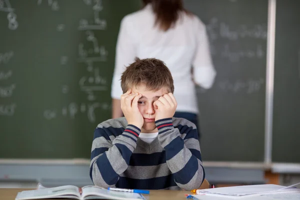 Student z rąk na twarz siedząc przy biurku — Zdjęcie stockowe