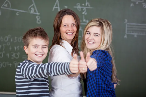 Profesor y estudiantes mostrando el gesto de pulgar contra pizarra — Foto de Stock