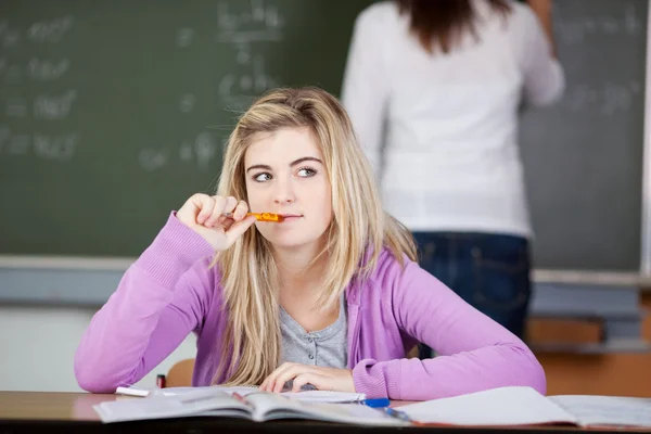 Nachdenkliche Studentin sitzt am Schreibtisch mit Lehrer im Backgr — Stockfoto
