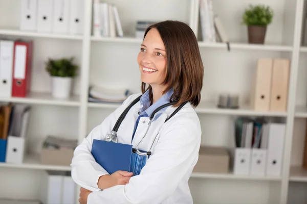 Doctor With Binder Looking Away Against Shelves — Stock Photo, Image