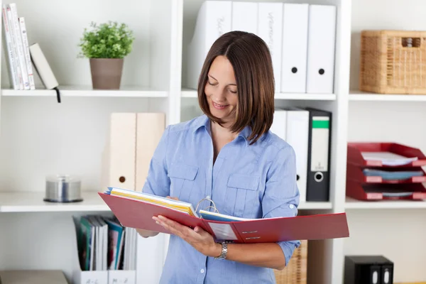 Zakenvrouw lezen van documenten in de binder tegen planken — Stockfoto