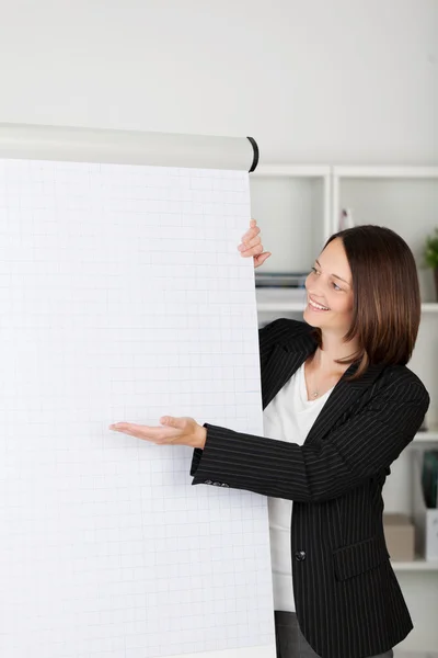 Mulher gesticular em direção a um flipchart em branco — Fotografia de Stock