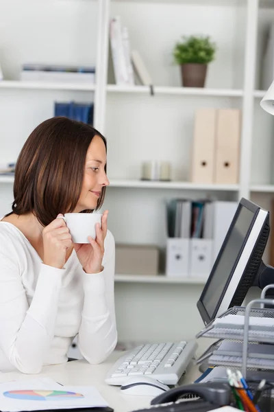 Бизнесвумен держит чашку кофе, глядя на компьютер — стоковое фото