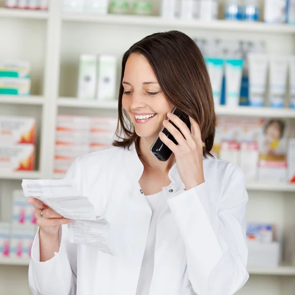 Farmacista in possesso di carta prescrizione durante l'utilizzo di telefono cordless — Foto Stock