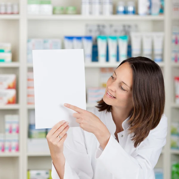 Kvinnliga farmaceut pekar på blankt papper på apotek — Stockfoto