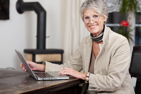 Donna anziana sorridente mentre lavora sul computer portatile — Foto Stock