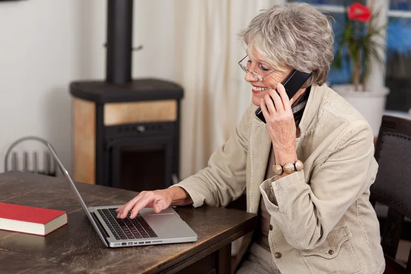 Pensionista feminina usando laptop e telefone móvel — Fotografia de Stock