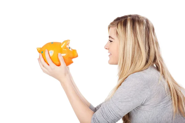 Teenage girl looking at piggy bank and smiling — Stock Photo, Image