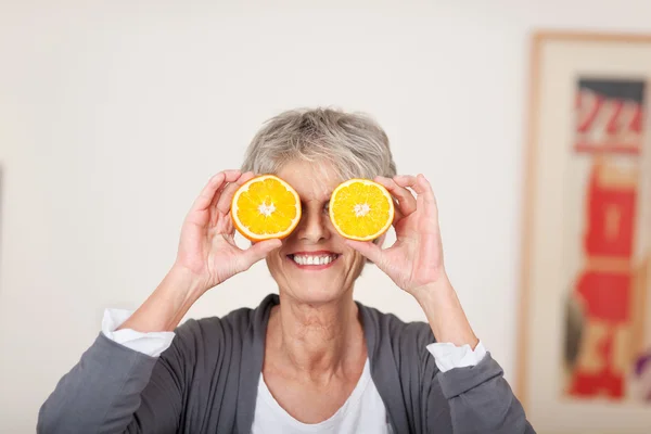 Ανώτερος γυναίκα που κρατά το μισό πορτοκάλια πάνω από τα μάτια — Φωτογραφία Αρχείου