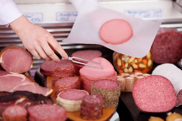 Rzeź pracownik sprzedaży plasterki salami — Zdjęcie stockowe