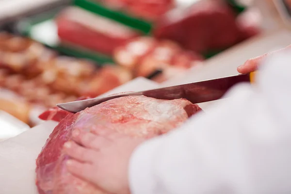 Mãos de açougueiro cortando carne com faca na loja — Fotografia de Stock