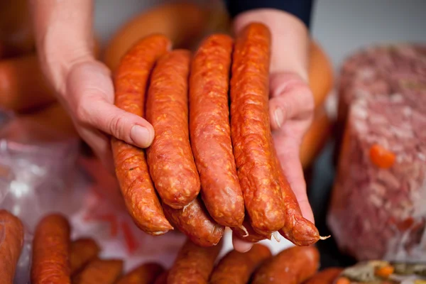 Mãos de açougueiro exibindo punhado de salsichas — Fotografia de Stock