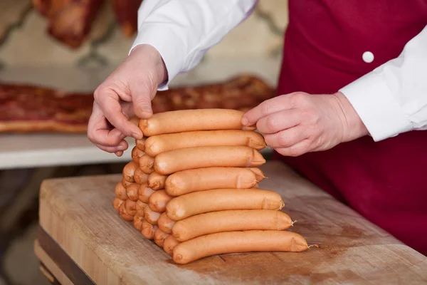 Boucher empilant des saucisses sur la table en bois — Photo