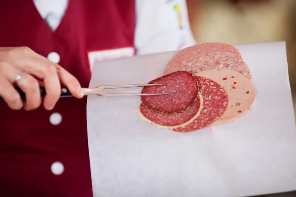 Mujer carnicera recogiendo salami con tenedor de carne — Foto de Stock